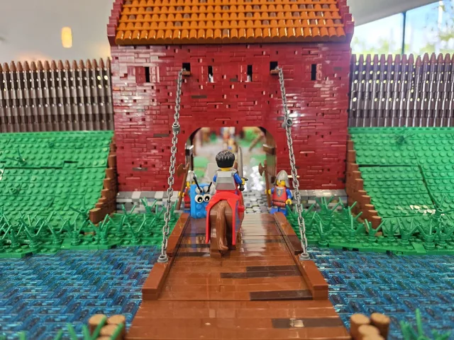 Close-up of a red LEGO castle gate with a wooden drawbridge over a moat